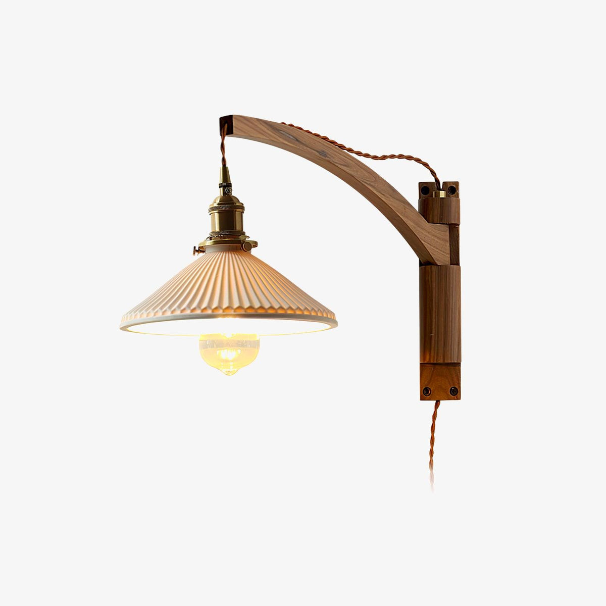 Plain backdrop view of this Clérachic wall light with a curved dark wood arm, brass socket, pleated white shade and twisted brown flex.