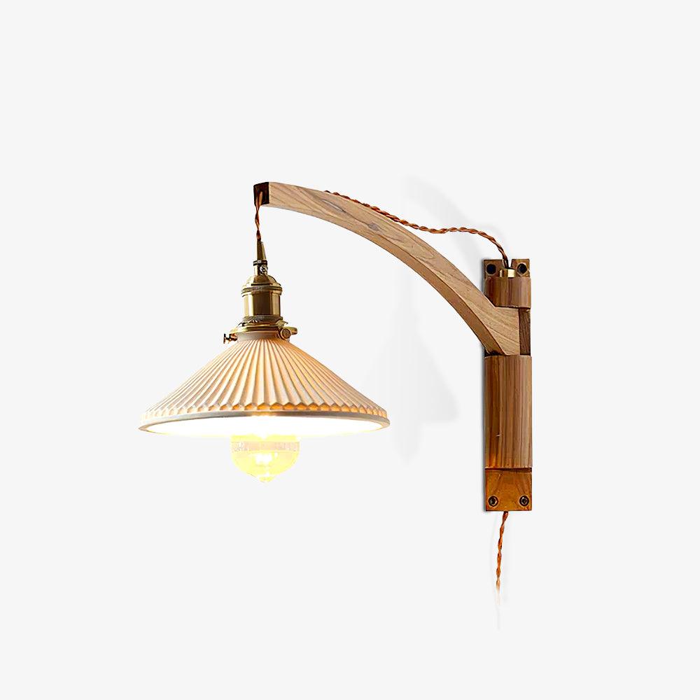 On a white backdrop, this Clérachic wall light has a curved light-wood arm and a pleated white shade with the bulb lit inside.