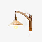 On a white backdrop, this Clérachic wall light has a curved light-wood arm and a pleated white shade with the bulb lit inside.