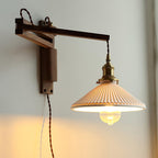 Angled view of the dark wood back plate and square arm of this Clérachic wall light, with the pleated shade lit warm below.