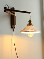 This Clérachic wall light on a pale wall, its dark walnut arm folded out and the pleated ceramic shade throwing a soft pool of light.