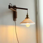 A Clérachic swing-arm wall light in warm light, the dark wood arm extended and the brass socket holding a glass bulb under the shade.