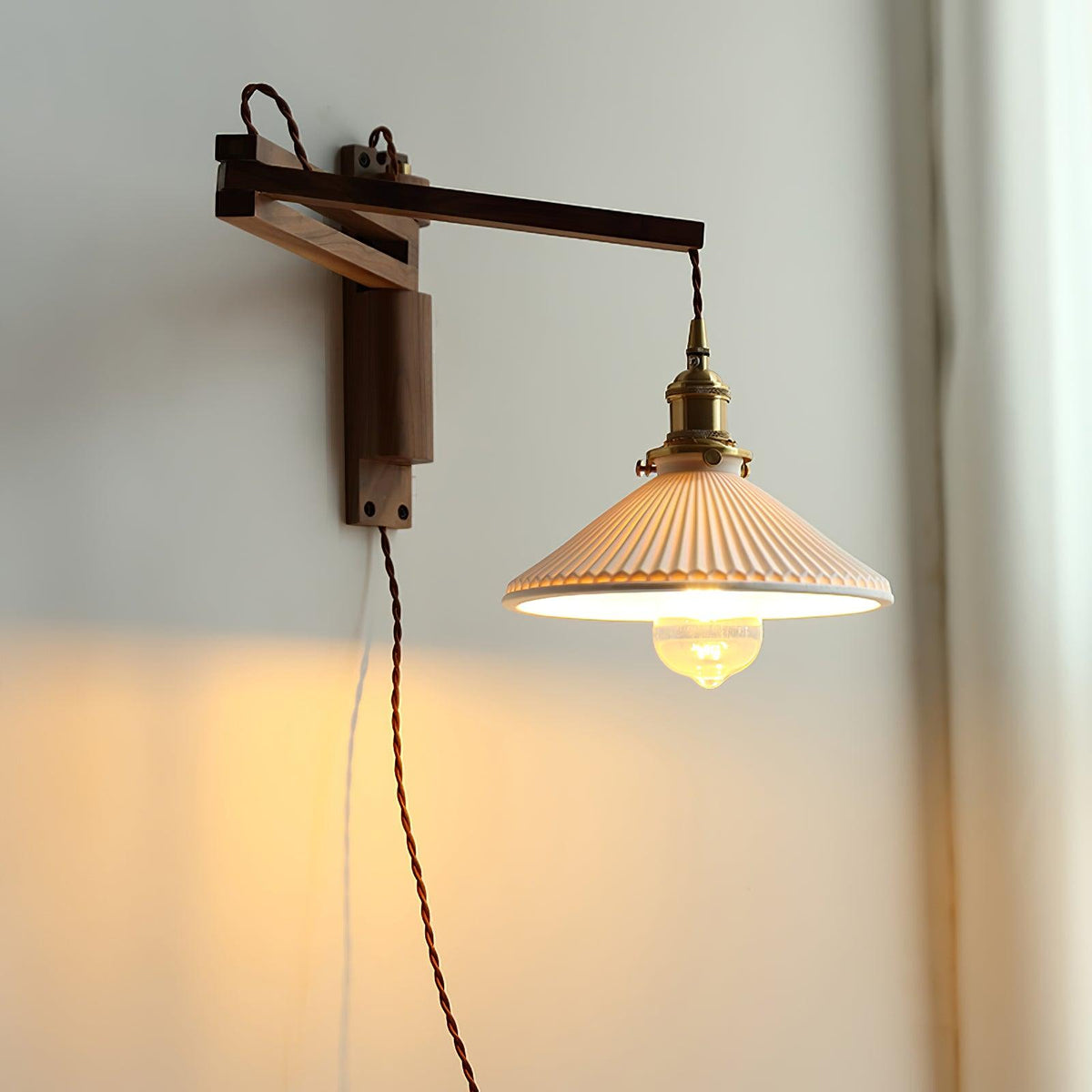 A Clérachic swing-arm wall light in warm light, the dark wood arm extended and the brass socket holding a glass bulb under the shade.