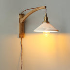 This Clérachic wall light with a pale ash-coloured curved arm, its pleated white shade casting a warm glow on a grey wall.