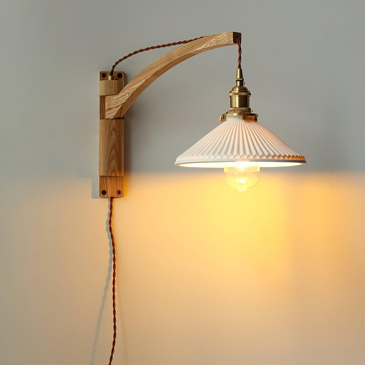 This Clérachic wall light with a pale ash-coloured curved arm, its pleated white shade casting a warm glow on a grey wall.
