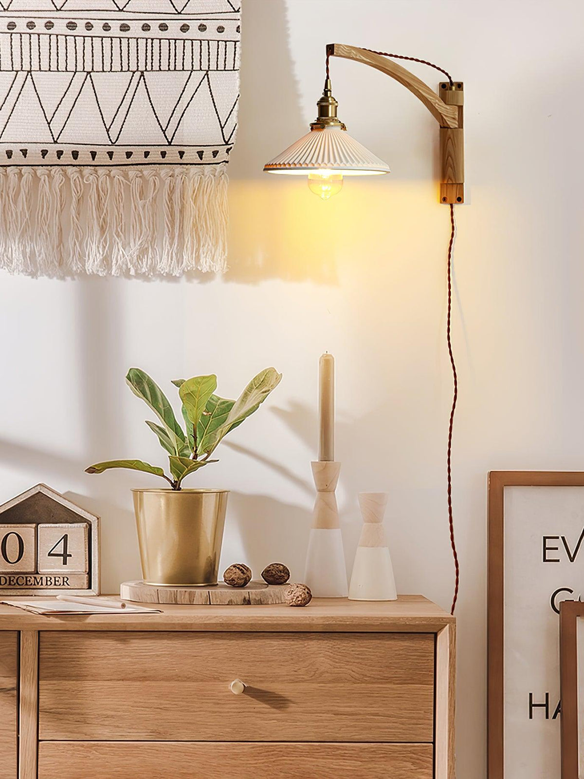 Higher up the wall, a Clérachic wall light with a curved arm lights a corner above a sideboard with a plant, a candle and a desk calendar.