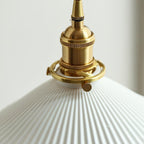 Close view of the knurled brass socket and the fine ribs of the pleated white ceramic shade on this Clérachic wall light.