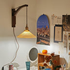 Over a cluttered pinboard wall and a small shelf, this Clérachic wall light lights a pleated shade in a warm glow from a dark curved arm.