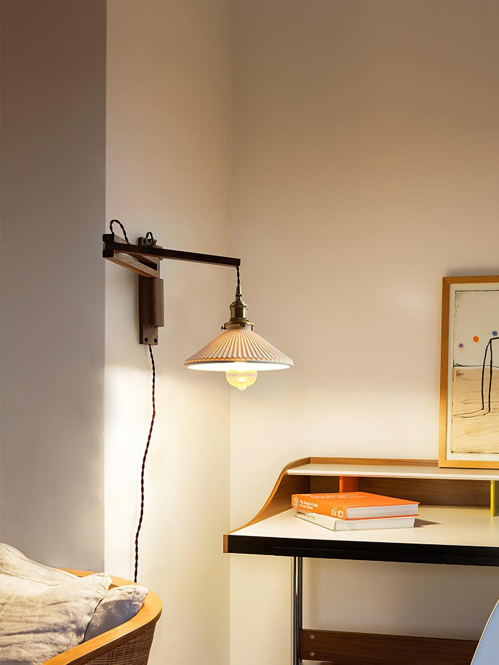 A Clérachic swing-arm wall light above a desk with books and a framed print, the pleated shade lit warm on a dark wood arm.