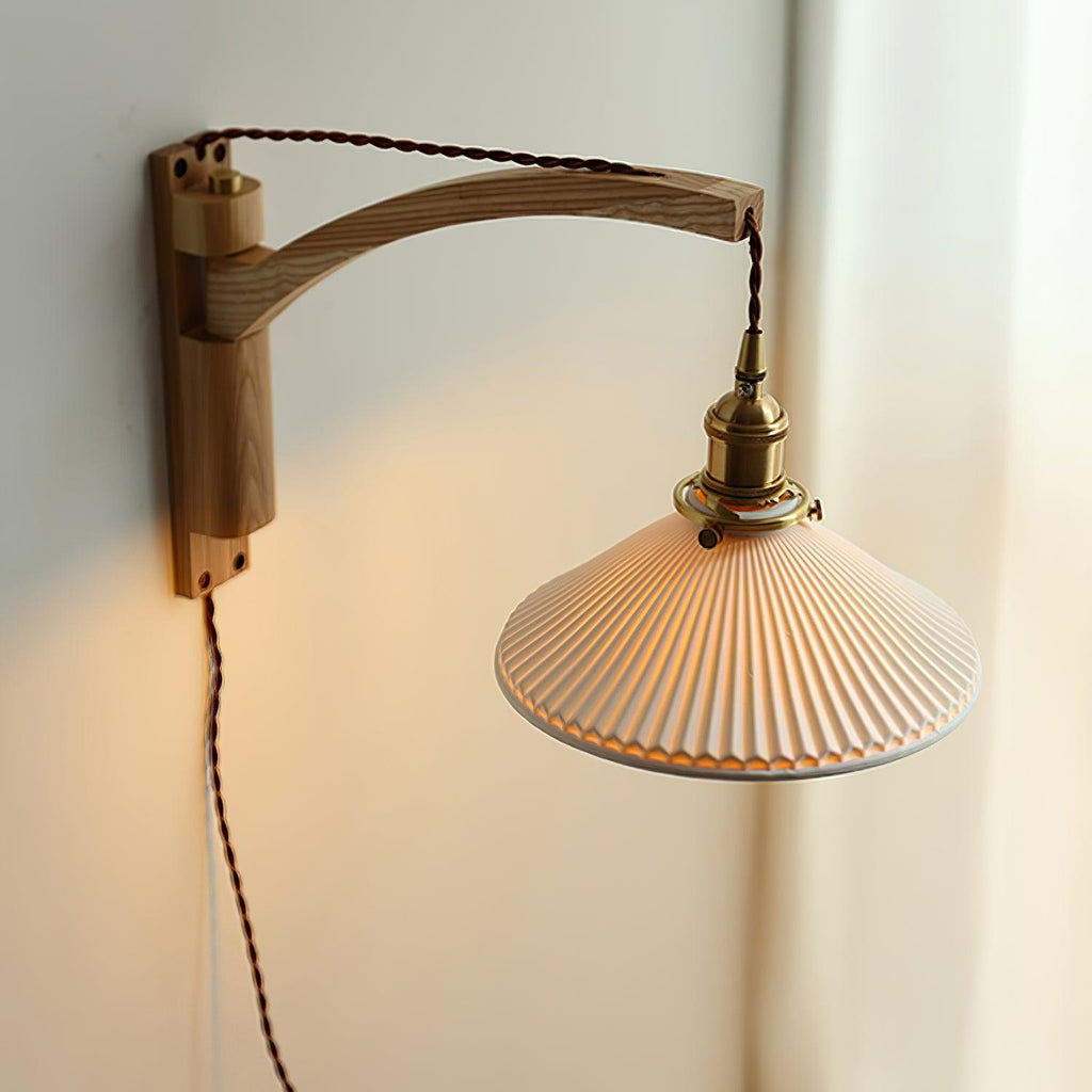 Close angle on the curved light-wood arm and pleated shade of this Clérachic wall light, glowing warm against a soft white curtain.