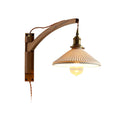 This Clérachic wall light on a plain white backdrop, its curved walnut arm meeting a pleated white shade and a visible bulb.