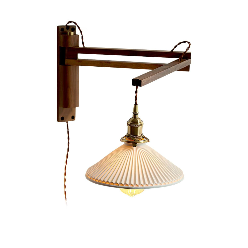 Walnut swing arm folded at a right angle on a white backdrop, holding the pleated shade of this Clérachic wall light.