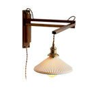 Walnut swing arm folded at a right angle on a white backdrop, holding the pleated shade of this Clérachic wall light.