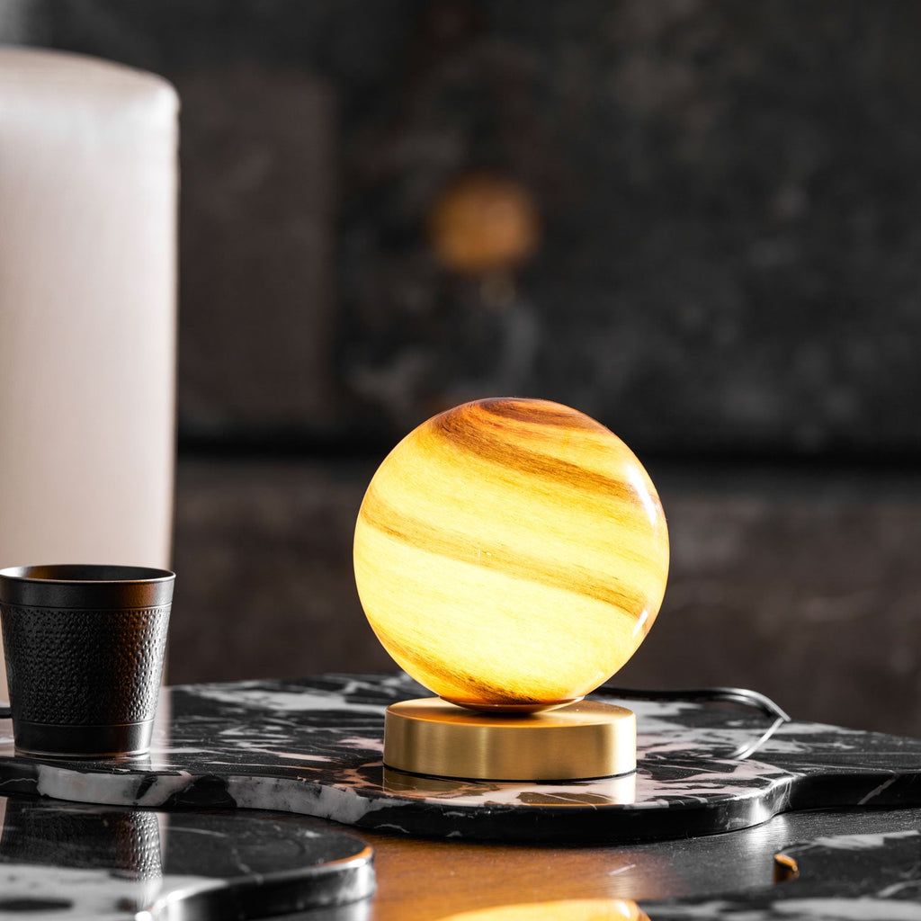 Lit amber-banded glass globe on a brass base, this Clérachic lamp sits on a black veined marble tray beside a black cup and a white pillar candle.