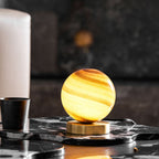 Lit amber-banded glass globe on a brass base, this Clérachic lamp sits on a black veined marble tray beside a black cup and a white pillar candle.