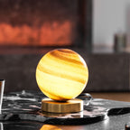 Close view of this Clérachic lamp glowing yellow and amber on a black-and-white marble tray, with a dark stone wall behind.