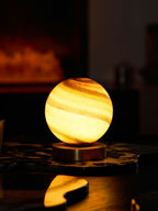 Portrait view of this Clérachic table lamp lit on a dark marble tray, its globe glowing against a blurred fireplace.