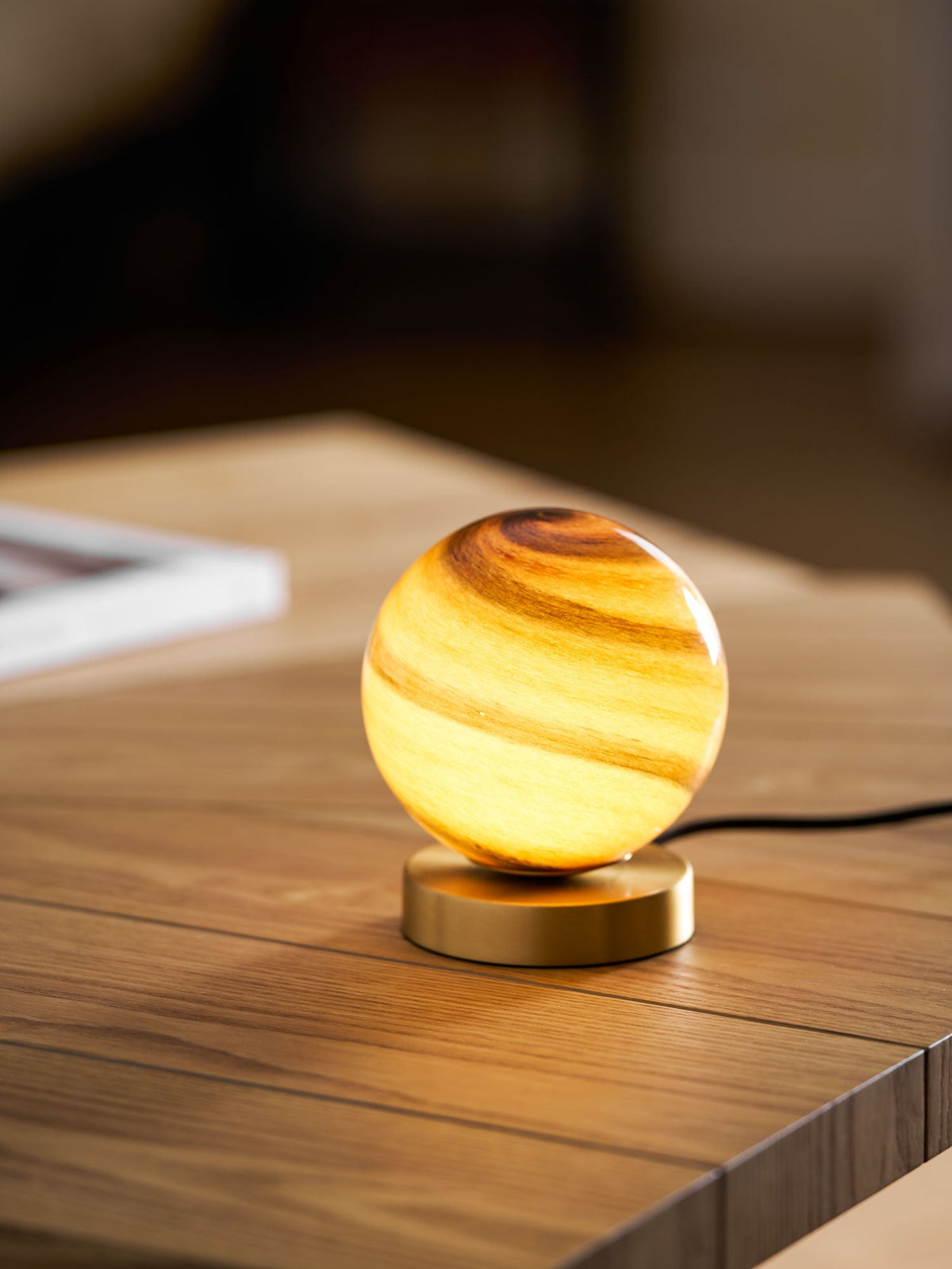 A small Clérachic globe lamp lit on a wooden table, its swirled amber glass above a low brass disc and a black cord.