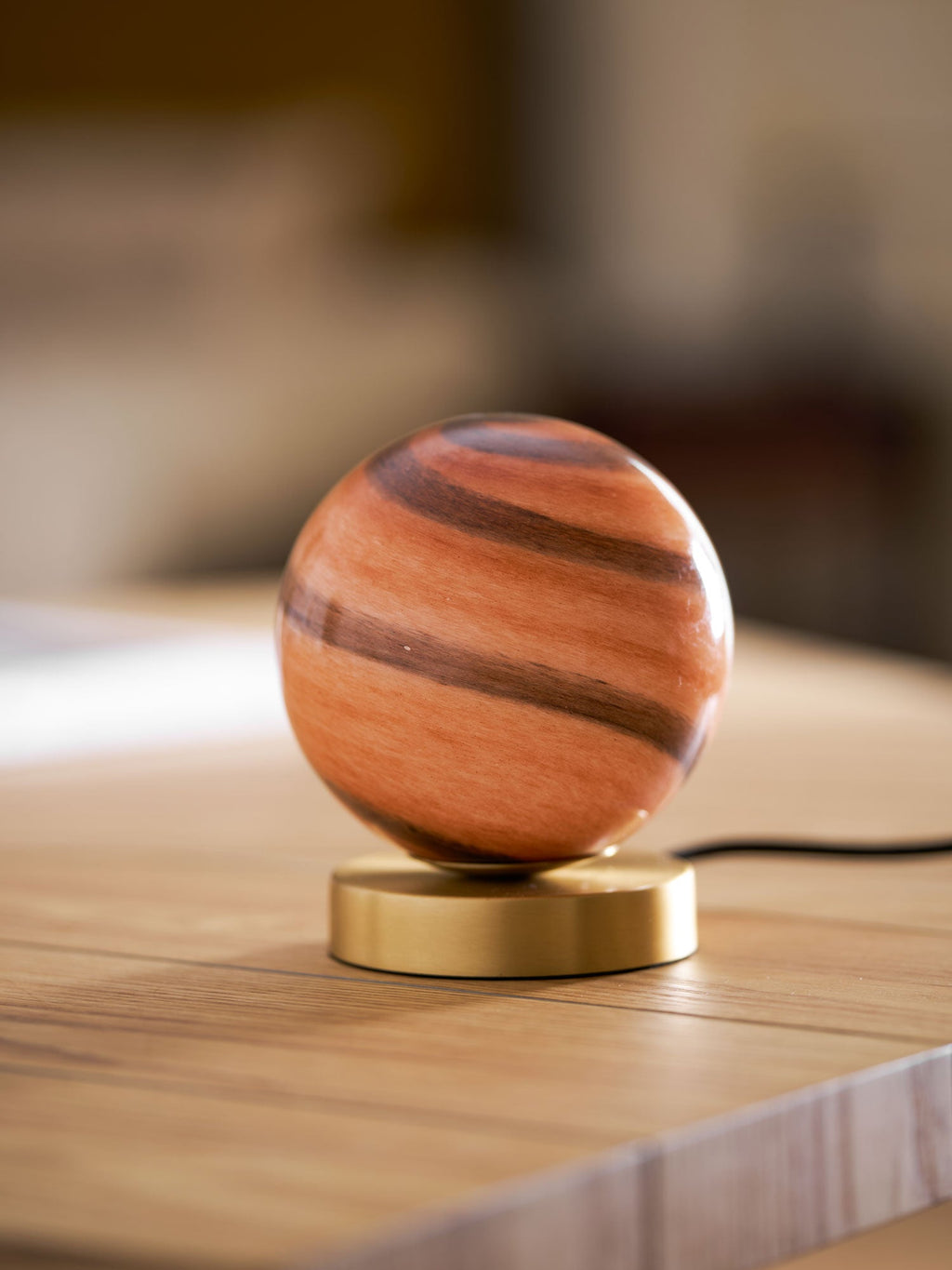 Unlit Clérachic globe lamp on a wooden table, its glass showing terracotta and brown bands above a brass base.