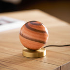 Low angle on this Clérachic globe lamp unlit, the terracotta and brown bands of the glass above a brass disc on pale wood.