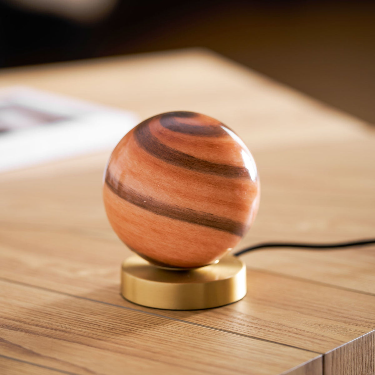 Low angle on this Clérachic globe lamp unlit, the terracotta and brown bands of the glass above a brass disc on pale wood.