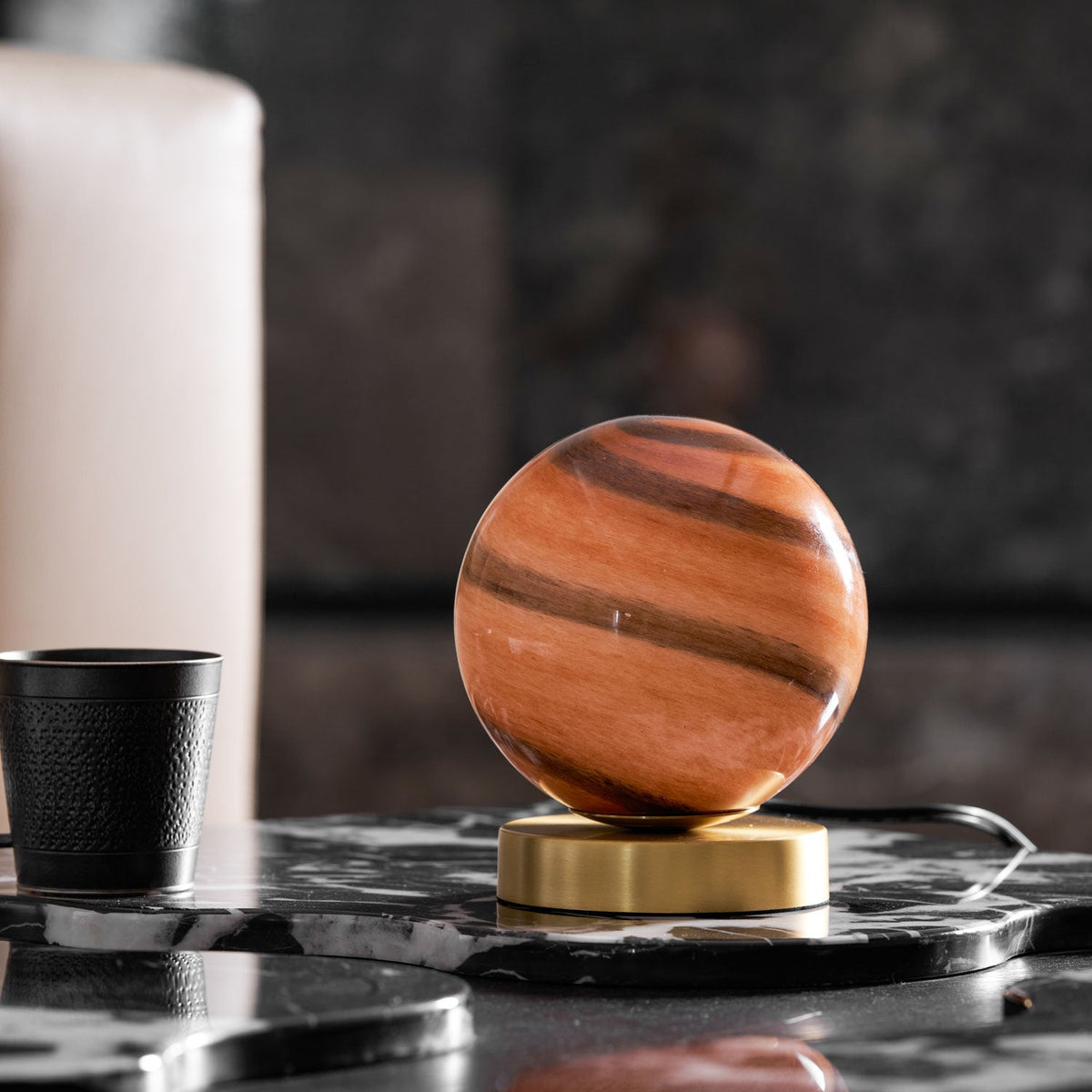 This Clérachic globe lamp unlit on a black marble tray, its terracotta-banded glass above a brass base, a black cup to the left.