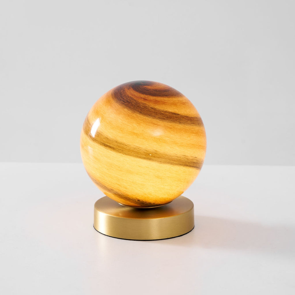 Clérachic globe lamp lit on a pale grey surface, amber and brown swirls in the glass above a round brass base.