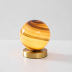 Clérachic globe lamp lit on a pale grey surface, amber and brown swirls in the glass above a round brass base.