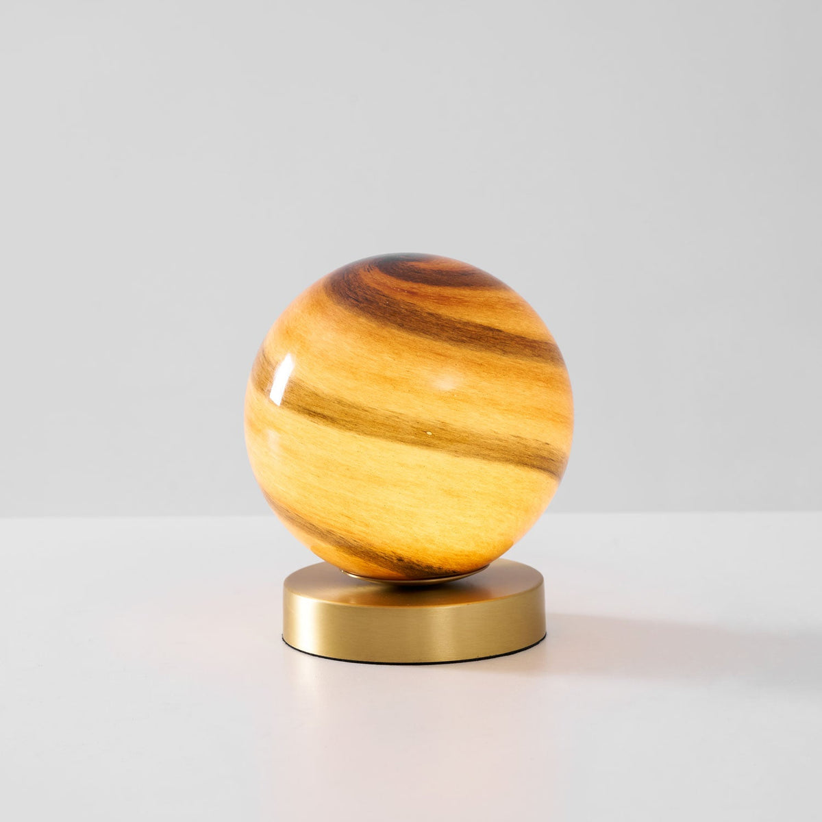 Side view of this Clérachic globe lamp lit on a light surface, the glowing amber glass above its brass base.