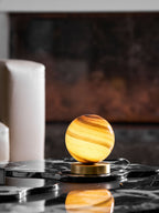 Distant view of this Clérachic lamp glowing on a black marble tray in front of a white armchair, its reflection in the stone below.