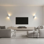 Two white Clérachic wall lights either side of a wall-mounted television in a pale living room with grey sofas.