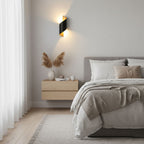 Black Clérachic wall light with a gold-toned inside above a floating bedside shelf and a bed with a beige throw.