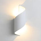 White Clérachic wall light lit against a pale wall, its twisted shell casting a soft glow above and below.