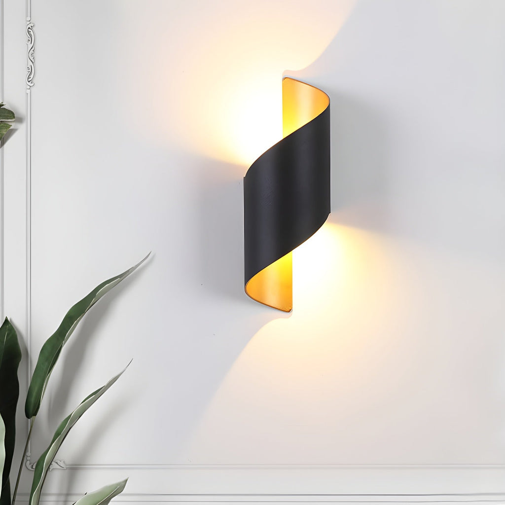Black Clérachic wall light with a gold-toned interior lit on a white wall, with a leafy plant at the edge of the frame.