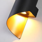 Close view of the lit gold-toned inside and the recessed light source of this black Clérachic wall light.