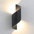 Lit Clérachic wall light on a grey wall, its dark twisted shell casting warm light both up and down.