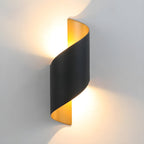 Side-on view of the black Clérachic wall light, its gold-toned inside glowing warm against a grey wall.