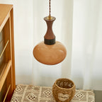 Clérachic Swirled Amber Glass Pendant Light hanging beside a cane-fronted cabinet, its walnut neck above a rounded caramel shade.