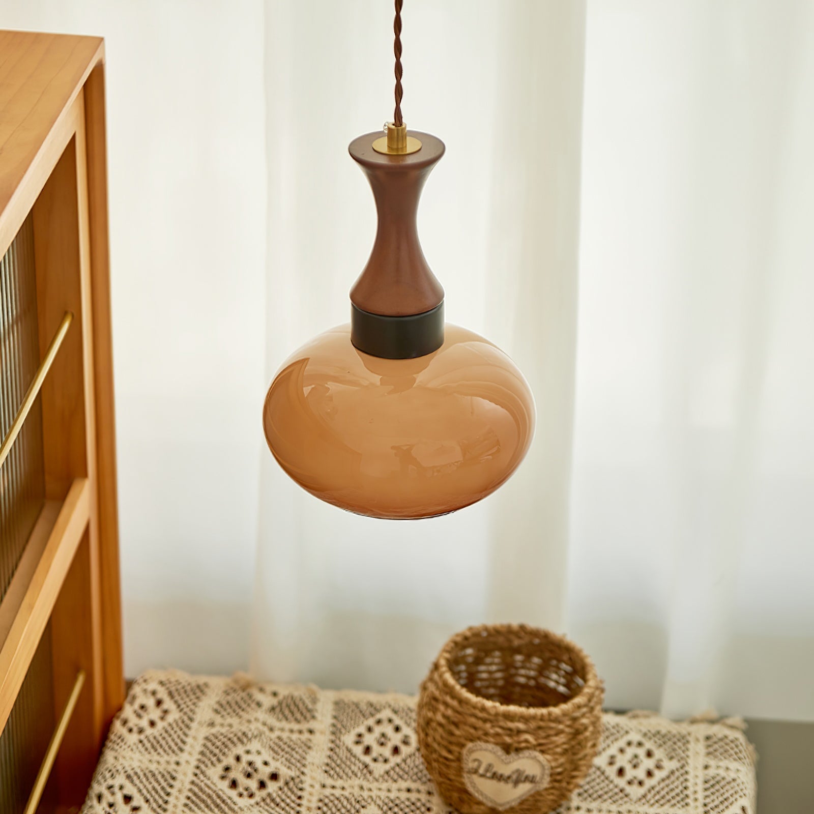 Clérachic Swirled Amber Glass Pendant Light hanging beside a cane-fronted cabinet, its walnut neck above a rounded caramel shade.