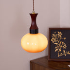 The Clérachic Swirled Amber Glass Pendant Light lit to a warm marigold beside a framed botanical print on a walnut sideboard.