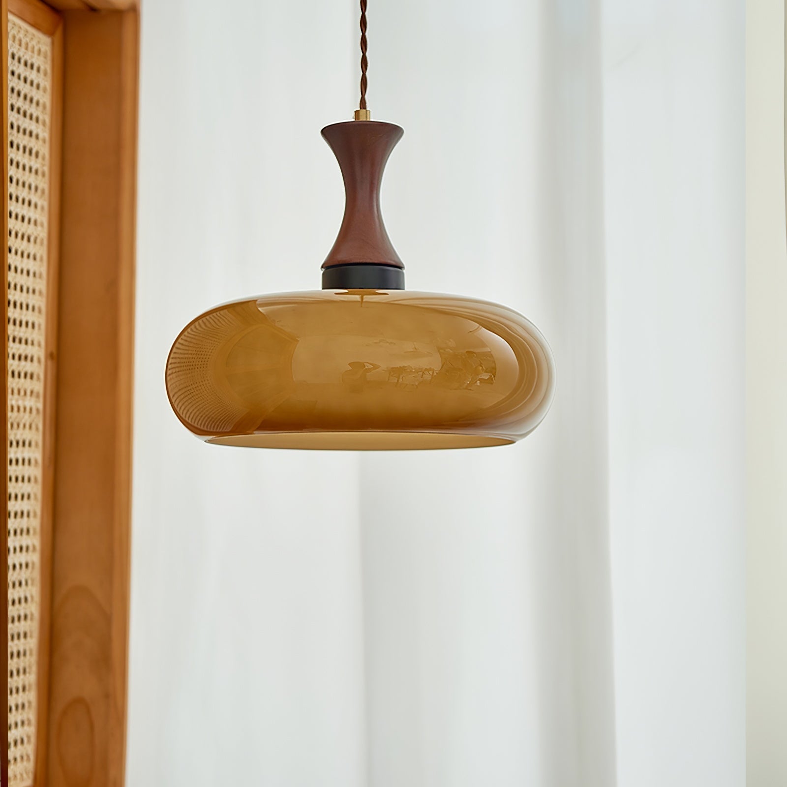 Clérachic Swirled Amber Glass Pendant Light in the wide shade, hung unlit against a sheer curtain beside a rattan screen.