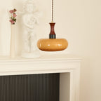 A Clérachic Swirled Amber Glass Pendant Light drops over a white fireplace mantel set with a cherub statue and dried roses.