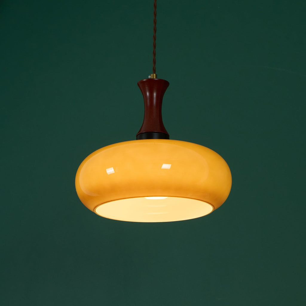 Clérachic Swirled Amber Glass Pendant Light lit against a deep green wall, the opal disc across the shade mouth glowing white.
