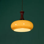 Clérachic Swirled Amber Glass Pendant Light lit against a deep green wall, the opal disc across the shade mouth glowing white.