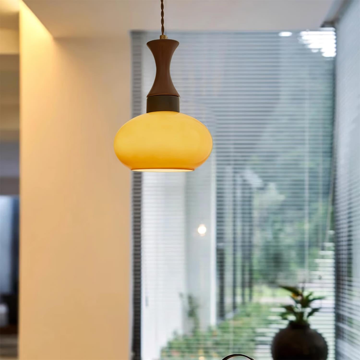 The small shade of the Clérachic Swirled Amber Glass Pendant Light lit in a hallway beside floor-to-ceiling louvred windows.