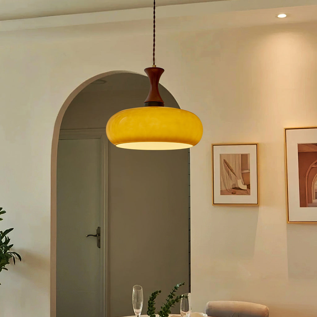 Clérachic Swirled Amber Glass Pendant Light hung low over a set dining table in an arched, art-hung room.
