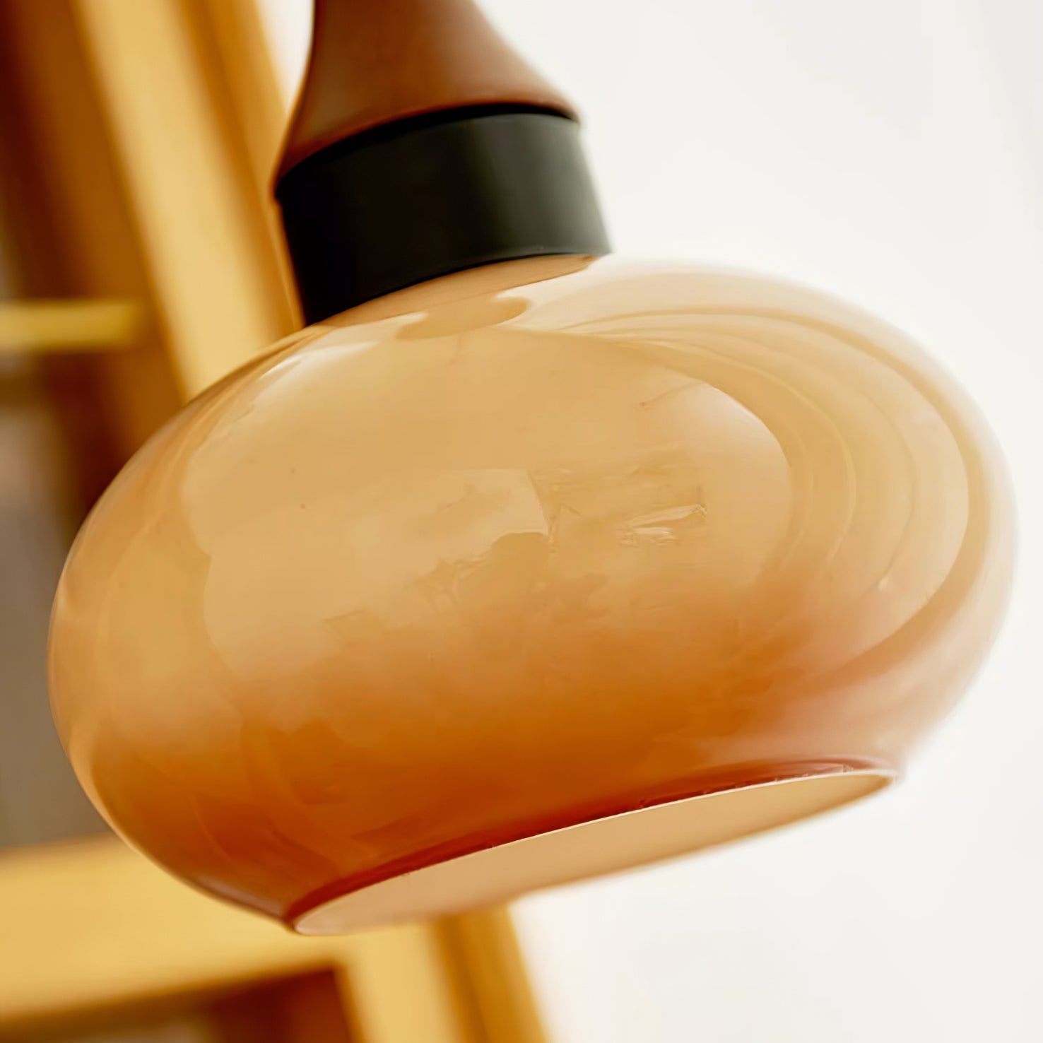Close view of a Clérachic amber glass pendant shade, cloudy swirls running through the blown glass under a matte black collar.