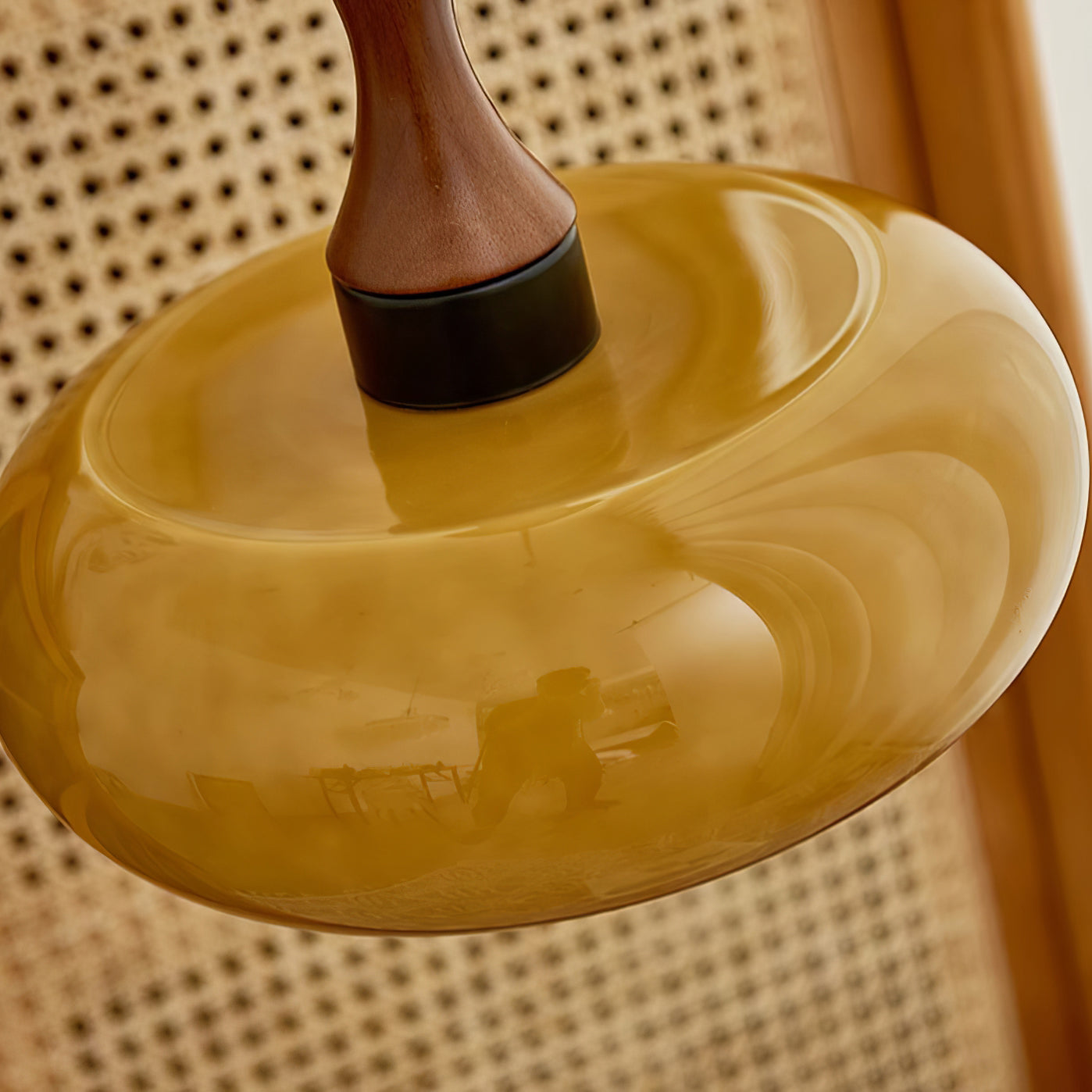 Overhead view of a Clérachic amber glass pendant, swirled striations circling the wide shade against a cane cabinet panel.