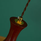 Detail of the brushed brass cord grip and set screw on the walnut neck of a Clérachic amber glass pendant, green backdrop.