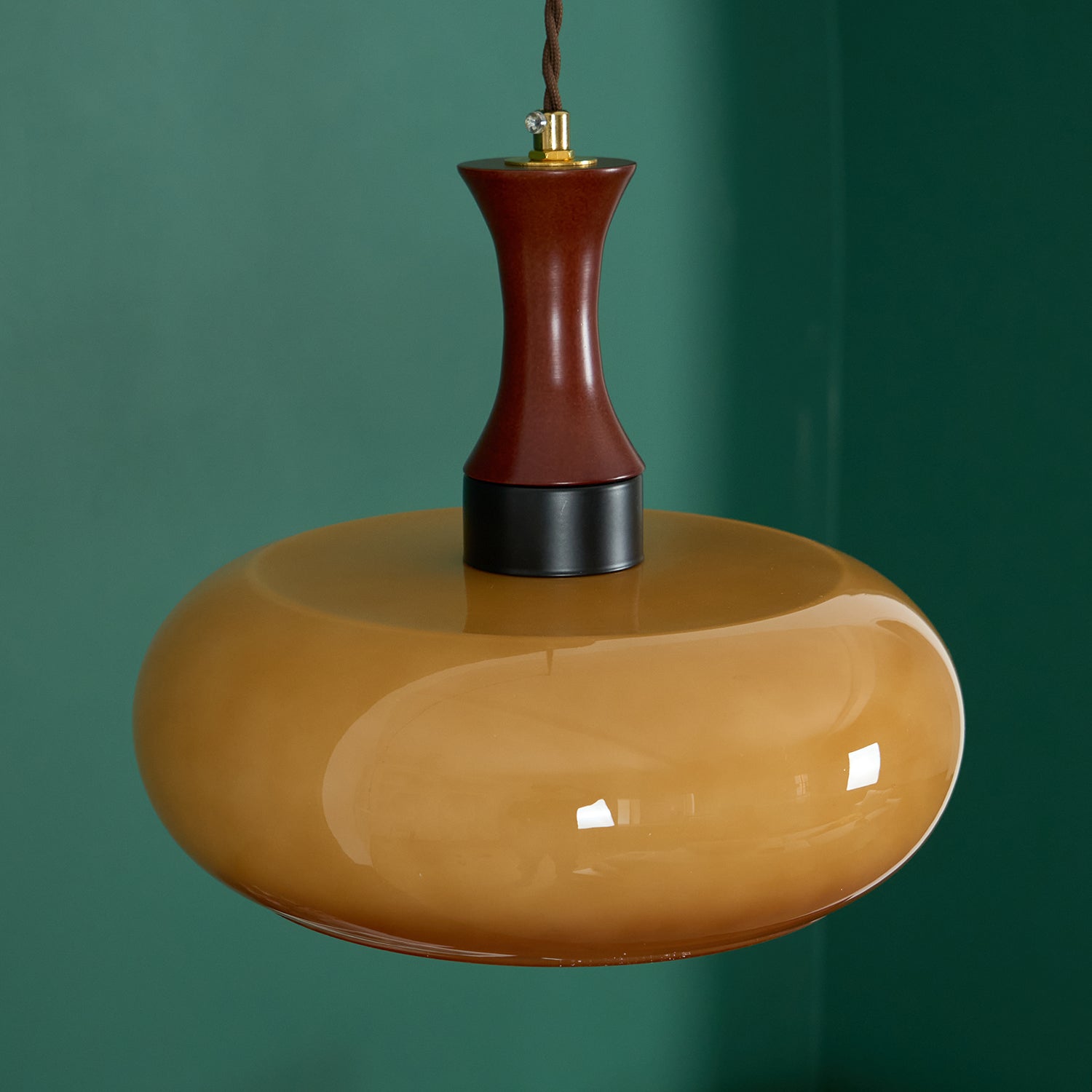 Clérachic Swirled Amber Glass Pendant Light photographed against a deep green wall, walnut neck and matte black collar in view.